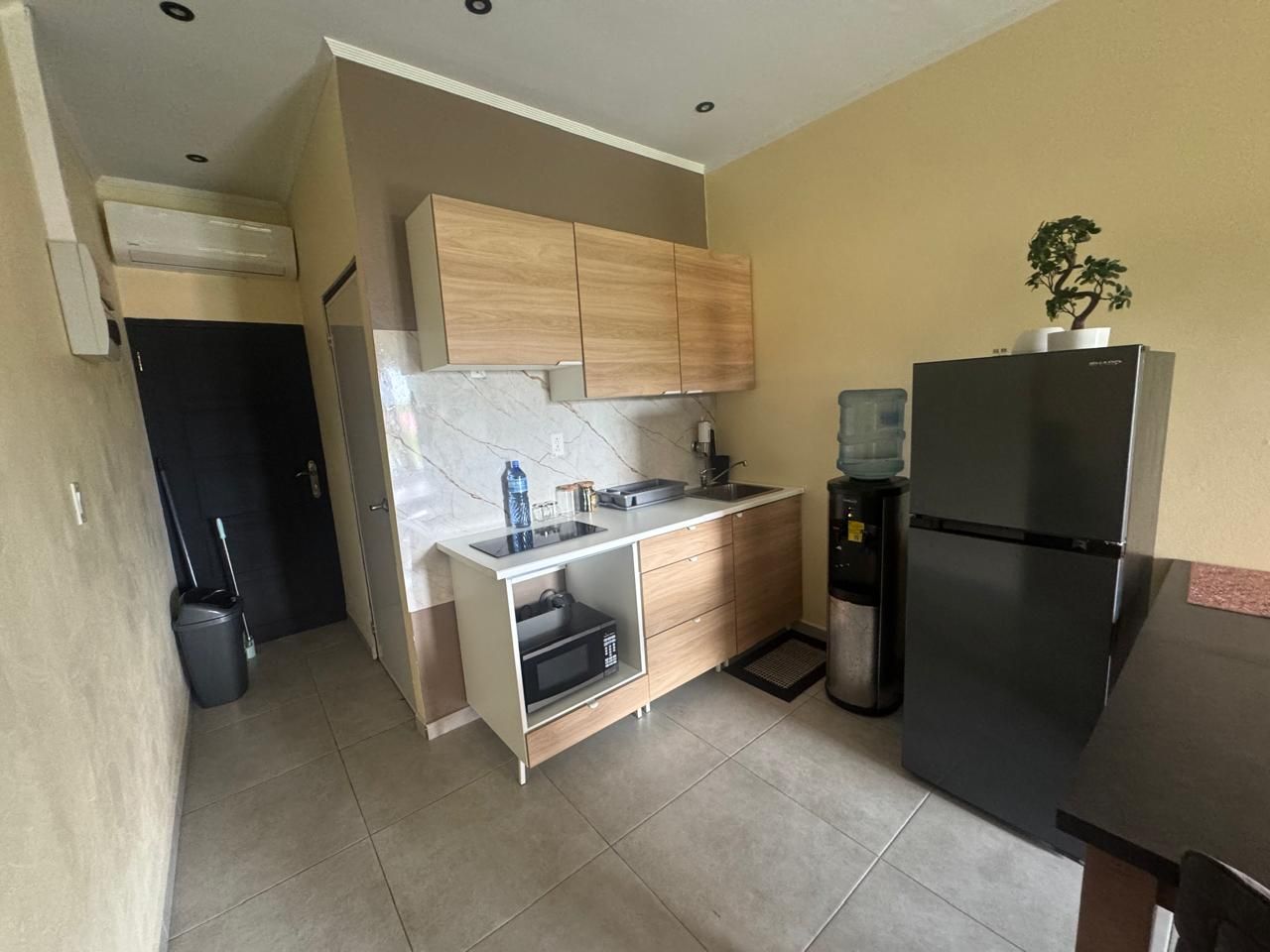 A compact kitchen with a built-in microwave, a water dispenser, and a black refrigerator.
