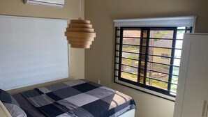 A bedroom with a bed, a window with a view, a hanging light fixture, and a white wardrobe. - Sisa Omi Appartments (Lelydorp)