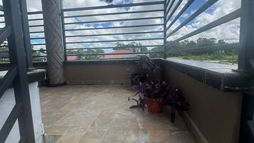 Varanda com piso de azulejos, grades de metal e plantas em vasos.