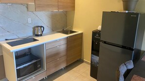 A compact kitchen with wooden cabinets, a built-in microwave, a sink, and a black refrigerator. - Sisa Omi Appartments (Lelydorp)