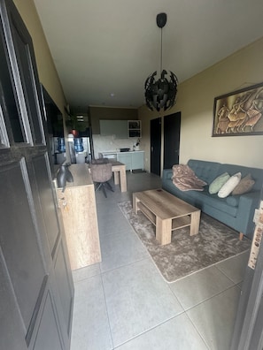 A modern living room with a sofa, coffee table, and a dining area with a kitchen in the background. - Sisa Omi Appartments (Lelydorp)