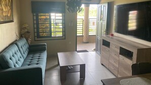A living room with a sofa, a coffee table, a TV, and a dining area with a table and chairs. - Sisa Omi Appartments (Lelydorp)