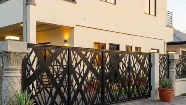 A modern building with a black metal fence, potted plants, and a paved entrance. - Sisa Omi Appartments (Lelydorp)