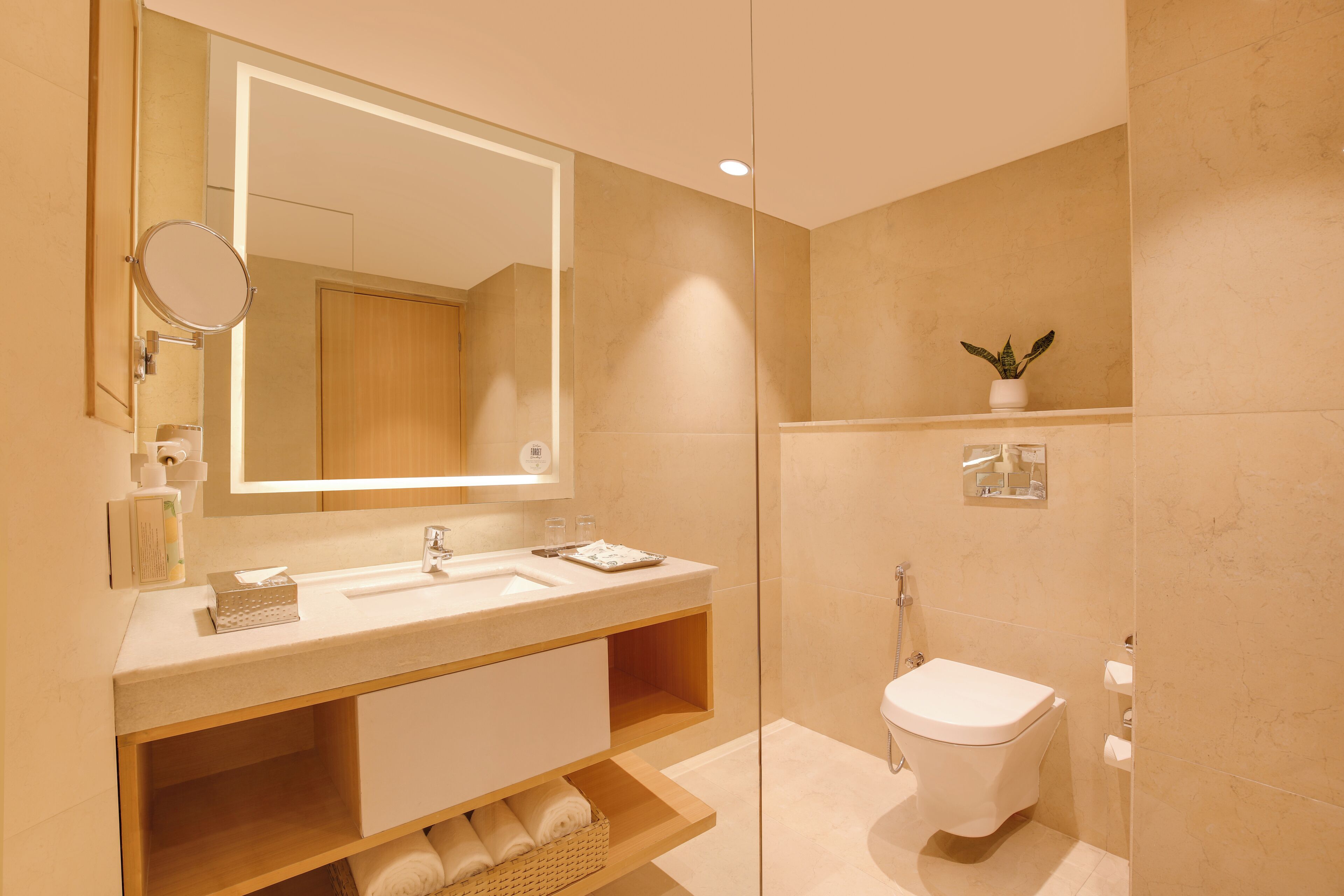 A modern bathroom with a large mirror, a sink, a toilet, and a small plant on the wall.