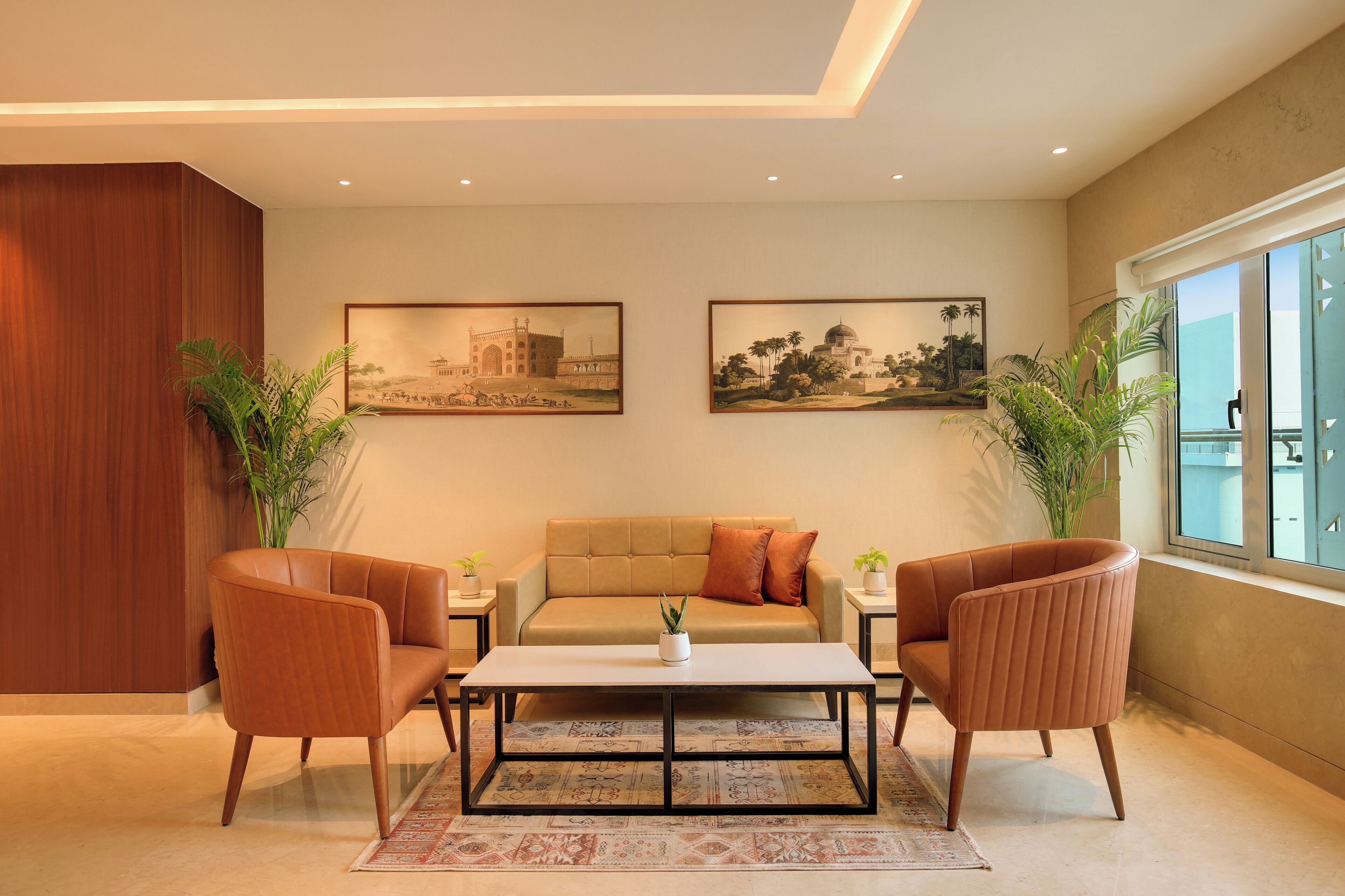 A modern living room with a beige sofa, two armchairs, a coffee table, and two paintings on the wall.