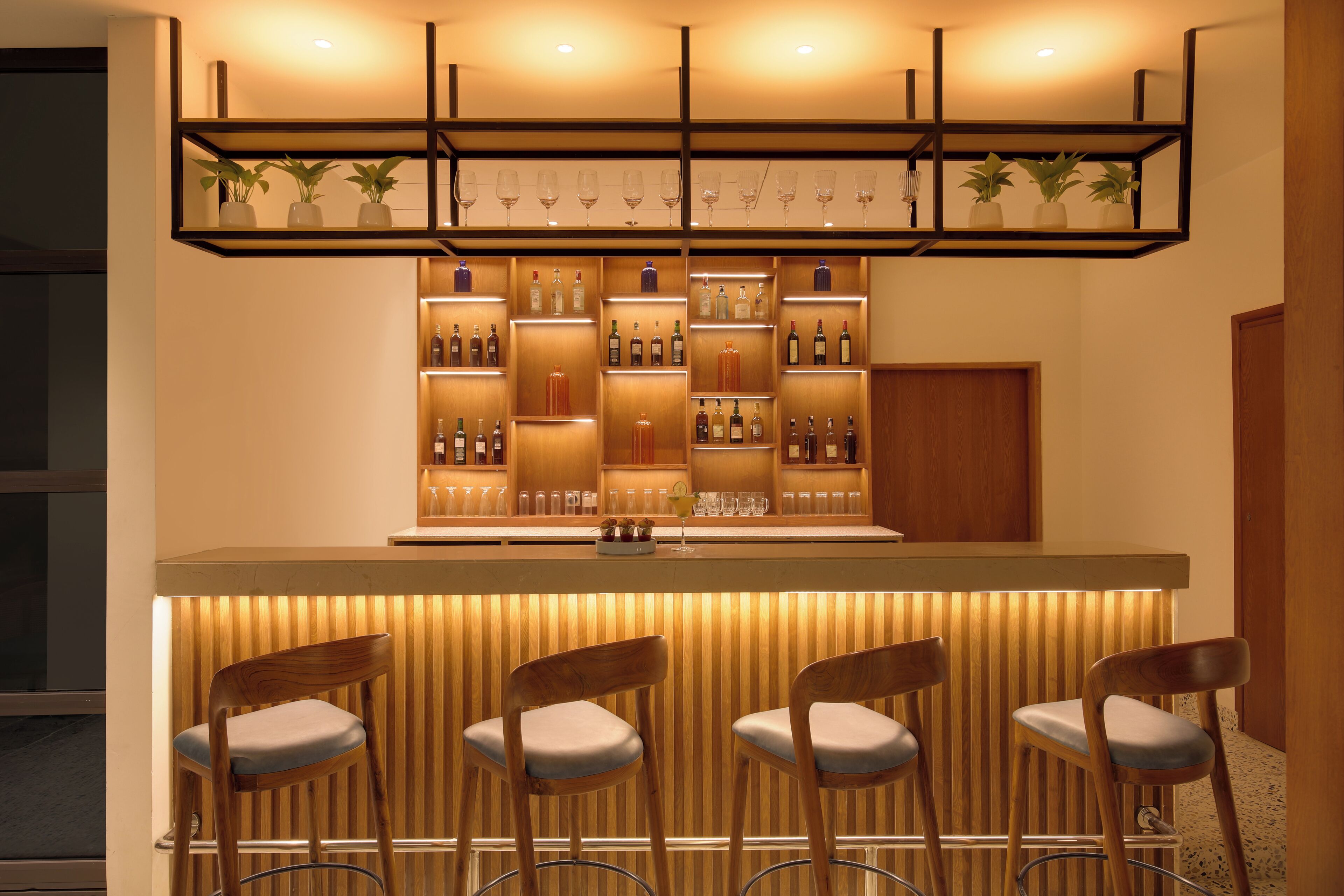 Un espace bar avec des chaises en bois, des étagères remplies de bouteilles et des plantes en pot.
