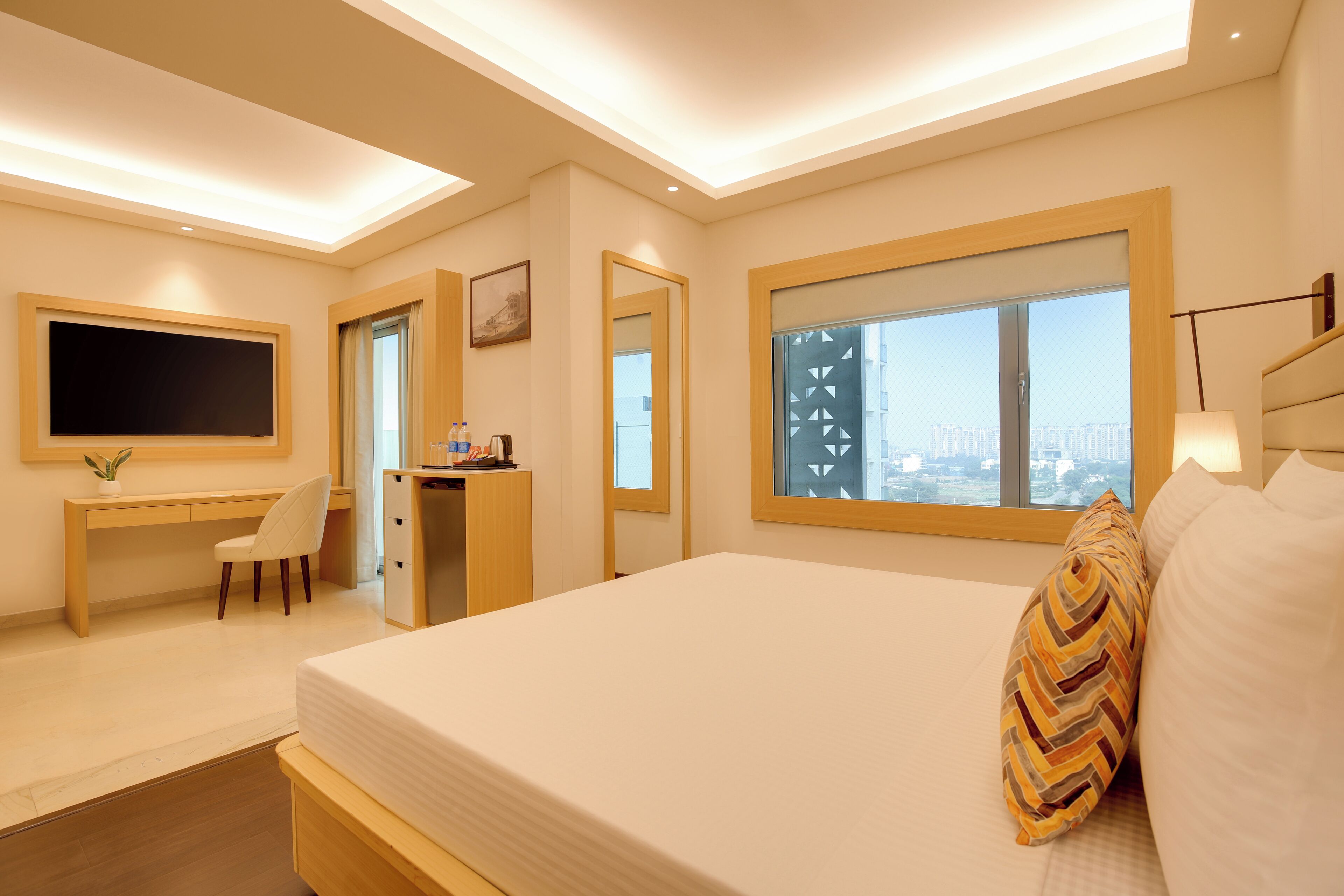 Una habitación de hotel moderna con una cama grande, un escritorio, una silla, un televisor y una ventana con vista a la ciudad.