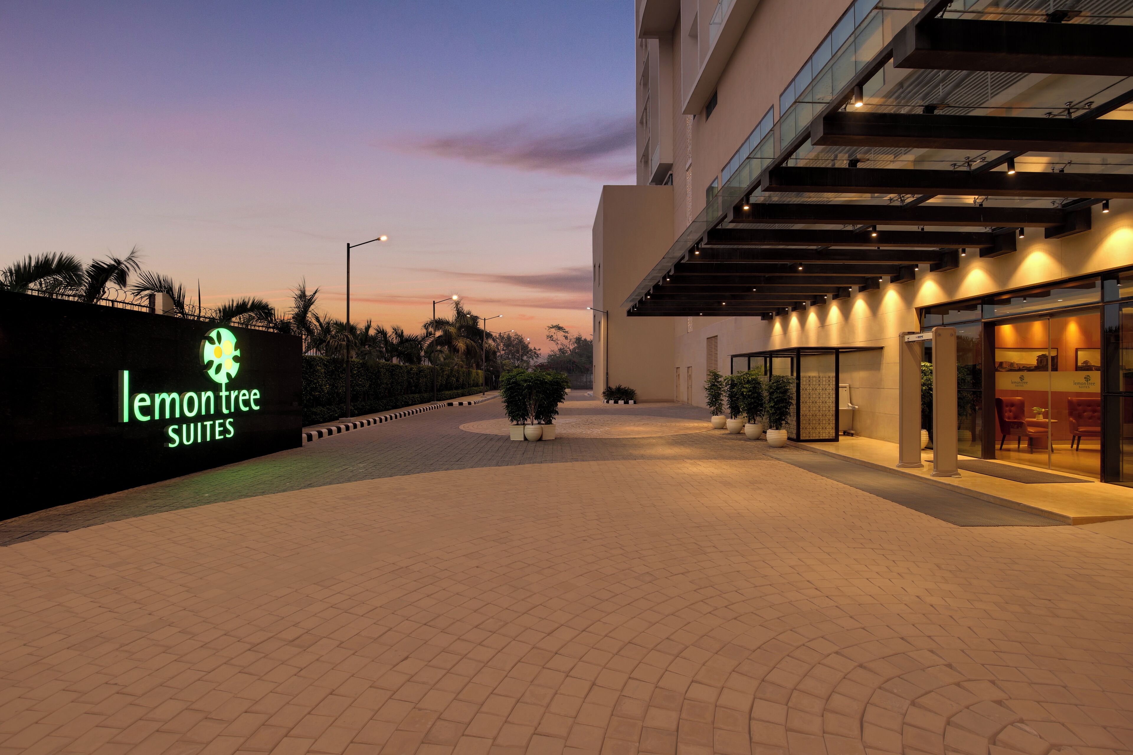 Entrada de hotel con un letrero que dice 'lemon tree suites' y un área exterior cubierta con asientos.