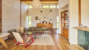 Un ampio soggiorno con soffitto in legno, un divano in pelle verde, una poltrona bianca, un tavolino da caffè e una lampada da terra moderna.