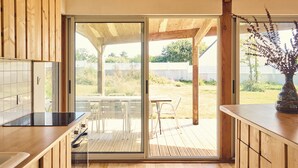 Una cucina moderna con mobili in legno, un piano di lavoro nero e una porta scorrevole in vetro che si apre su un patio esterno con tavolo e sedie.