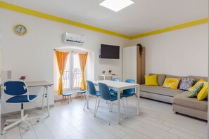 A modern living room with a dining area, a sofa with colorful cushions, a flat-screen TV, and a clock on the wall. - Pino Baroque Near Beach Etna by Wonderful Italy (Catania)