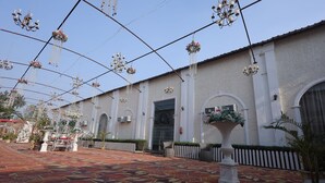 Ein Innenhof mit gemustertem Boden, hängenden Blumendekorationen und einem Gebäude mit Rundbogenfenstern und einem weißen Zaun.