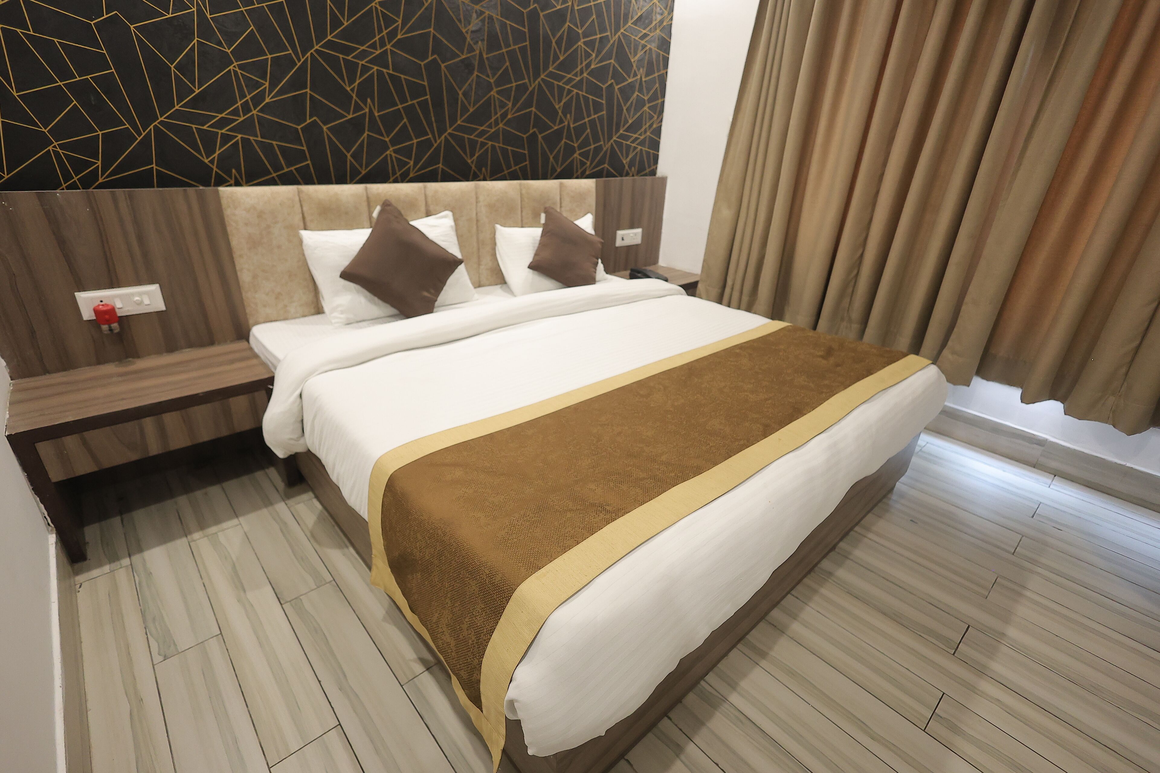 A hotel room with a large bed, a wooden headboard, a nightstand, and a modern wall design.