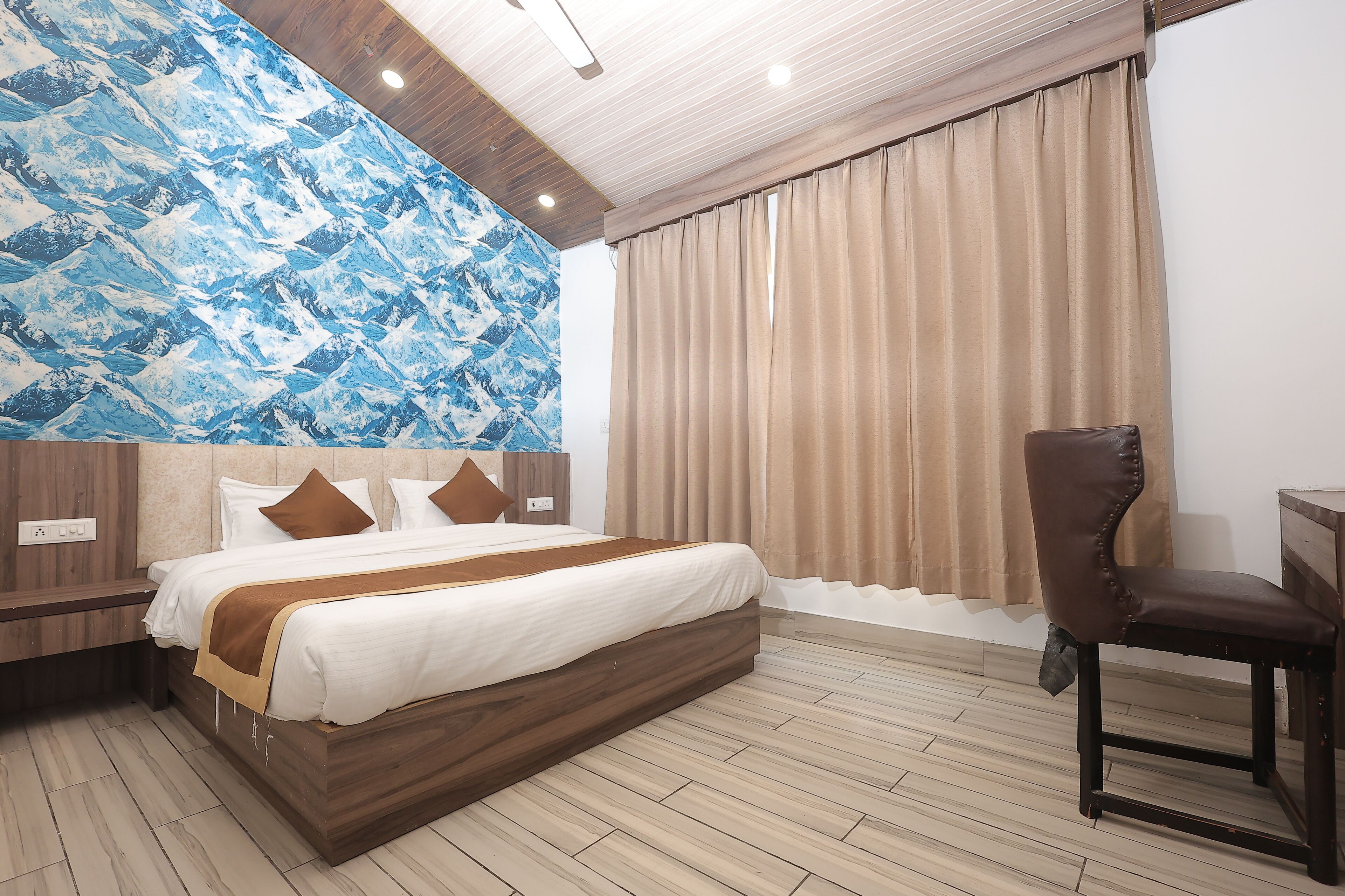 A hotel room with a large bed, a wooden headboard, a desk, and a chair.