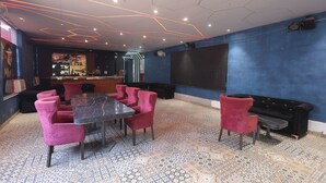 Ein Zimmer mit einem gemusterten Boden, einem schwarzen Tisch mit Stühlen, einer Bar und einem großen schwarzen Bildschirm an der Wand.