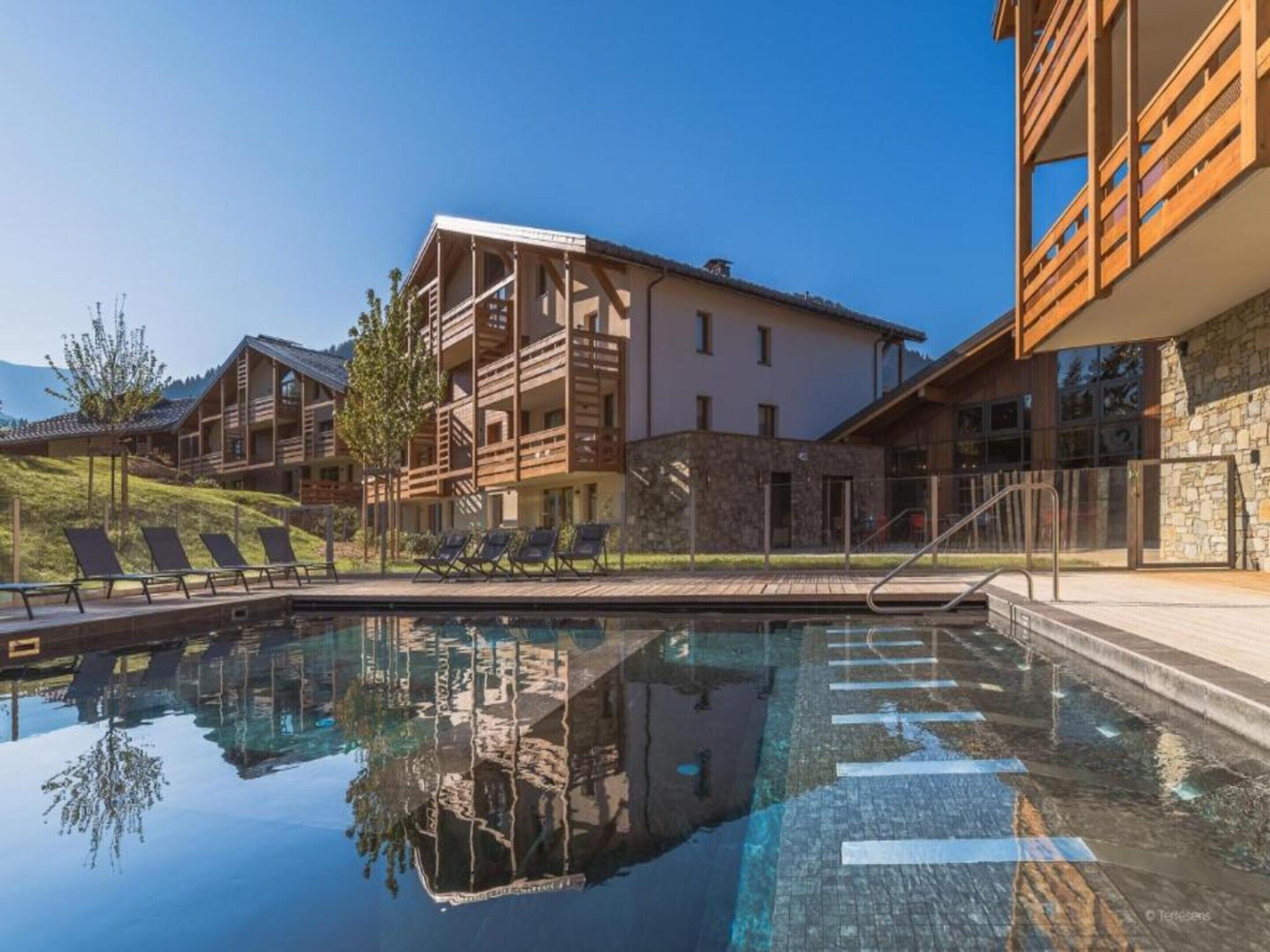 A pool area with lounge chairs, a stone building, and a wooden structure with balconies.