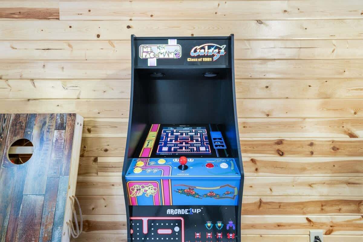 Un plancher en bois sur lequel se trouve une borne d’arcade noire, portant les inscriptions « Arcade 1UP » et « Promotion 1981 ».