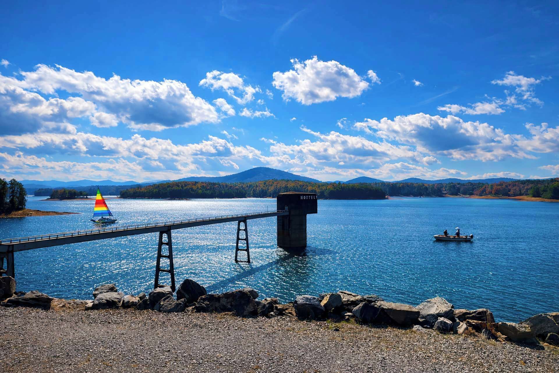 A lake with a bridge, a sailboat, and a dock.