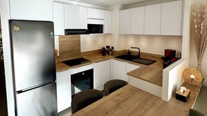 Una cocina moderna con armarios blancos, un refrigerador de acero inoxidable, una encimera de madera y un comedor con mesa y sillas.