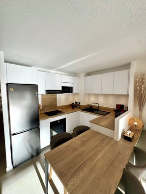 A modern kitchen with white cabinets, a stainless steel refrigerator, a wooden countertop, and a dining area with a table and chairs. - 2-bedroom condo in soothing Orient Bay. (Orient bay)
