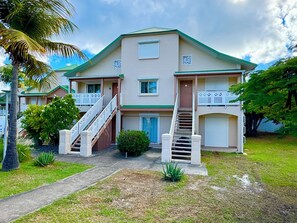 A two-story building with a green roof, white balconies, and a central staircase. - 2-bedroom condo in soothing Orient Bay. (Orient bay)
