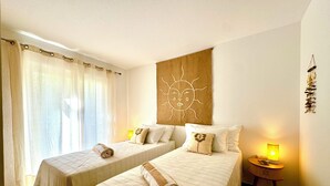 Habitación de hotel con dos camas, un adorno mural con motivos de sol y una mesita de noche pequeña con lámpara.