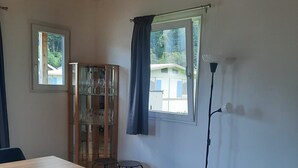 Ein Zimmer mit Holzboden, einem Esstisch mit Stühlen, einem Sofa, einer Stehlampe und einem Fenster mit Vorhängen.