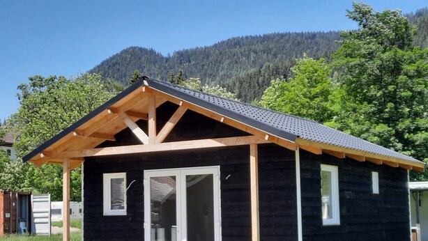 Eine Holzdiele mit überdachter Veranda und großen Glasüren, vor einer Bergkulisse gelegen.