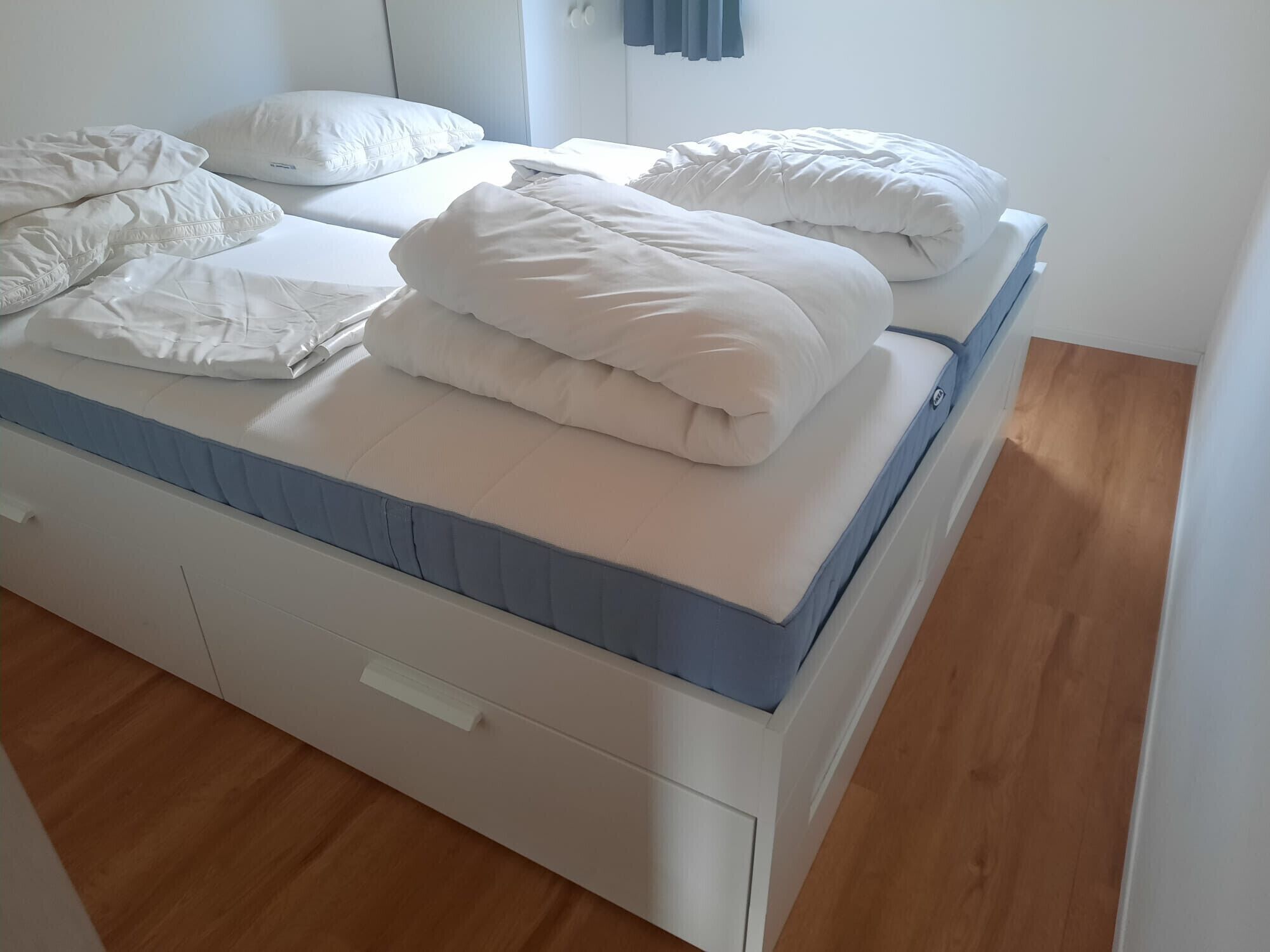 Een net opgemaakt bed met witte beddengoed en een blauwe matrasbeschermer.