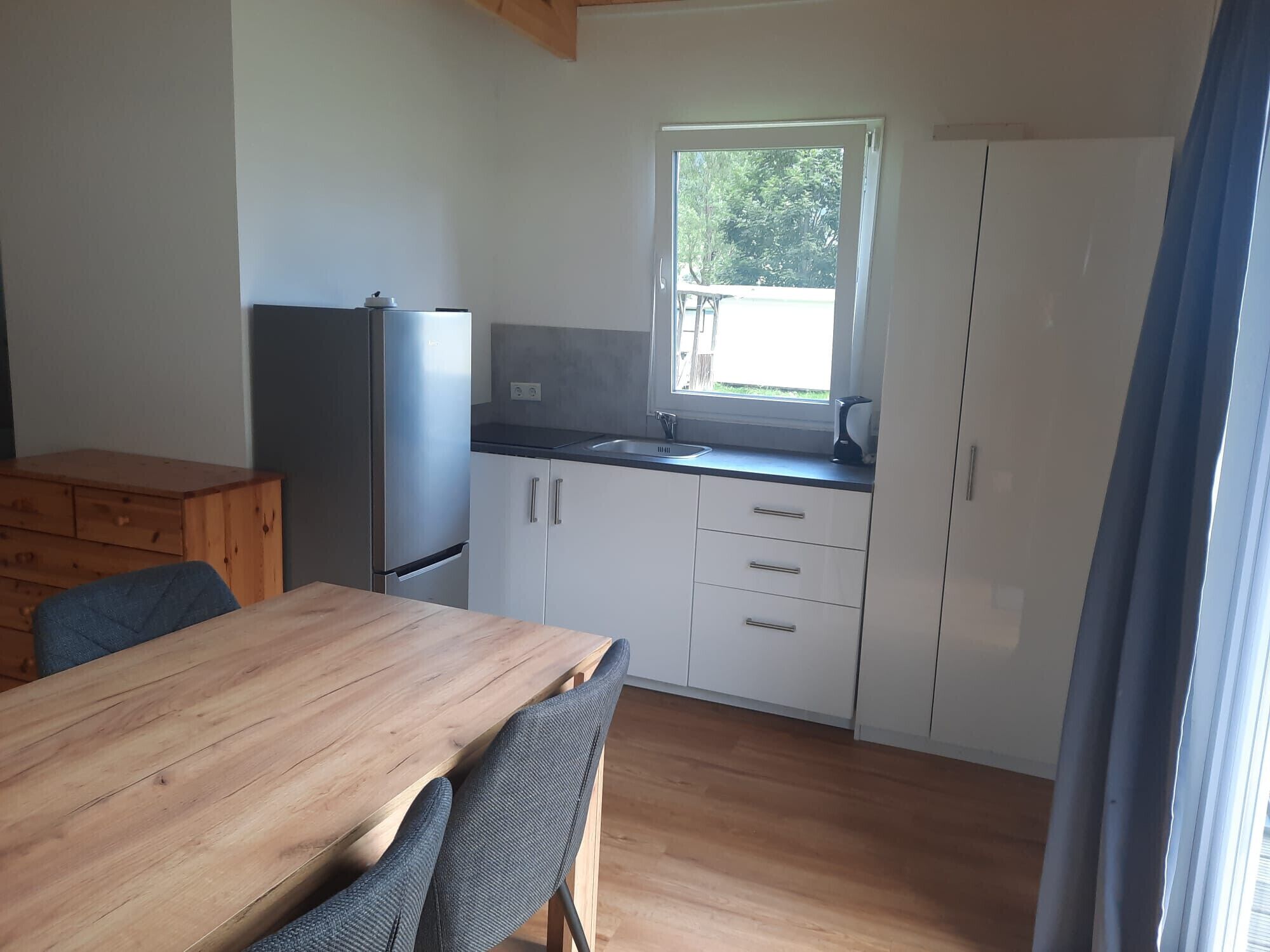 Una cocina compacta con una mesa de madera, sillas, un refrigerador y armarios.