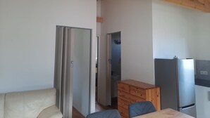 Eine kleine Küche mit einem Edelstahlkühlschrank, einem Holzschrank und einem beigen Sofa.