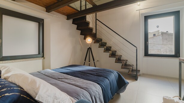A bedroom with a bed, a window, a staircase, and a tripod lamp. - Comfort Quadruple Room with Mountain View, Wi-Fi and Air Conditioning (Calangianus)