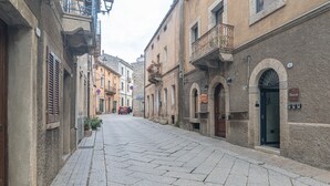 A narrow street lined with historic buildings, a red car parked on the side, and a no parking sign. - Comfort Quadruple Room with Mountain View, Wi-Fi and Air Conditioning (Calangianus)