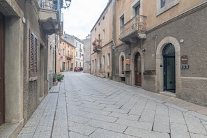 A narrow street lined with historic buildings, a red car parked on the side, and a no parking sign. - Comfort Quadruple Room with Mountain View, Wi-Fi and Air Conditioning (Calangianus)