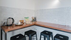 A kitchen with a wooden countertop, four black stools, a kettle, a framed picture, and a vase with flowers. - Comfort Quadruple Room with Mountain View, Wi-Fi and Air Conditioning (Calangianus)