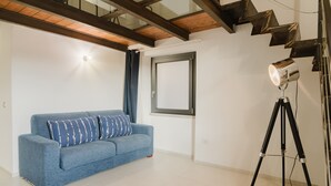 A room with a blue sofa, a tripod with a light, and a window with a curtain. - Comfort Quadruple Room with Mountain View, Wi-Fi and Air Conditioning (Calangianus)
