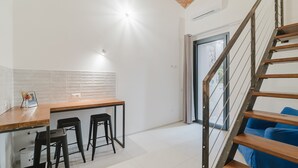 Une cuisine moderne avec un comptoir en bois, des tabourets de bar noirs et un escalier agrémenté de coussins bleus.