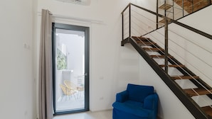 Un intérieur moderne avec un escalier, un canapé bleu et une porte vitrée donnant sur un espace extérieur.