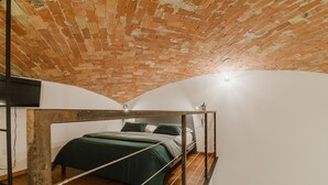 Une chambre à coucher aménagée dans un grenier, avec un plafond en briques, un lit recouvert d’une literie verte et un plancher en bois.