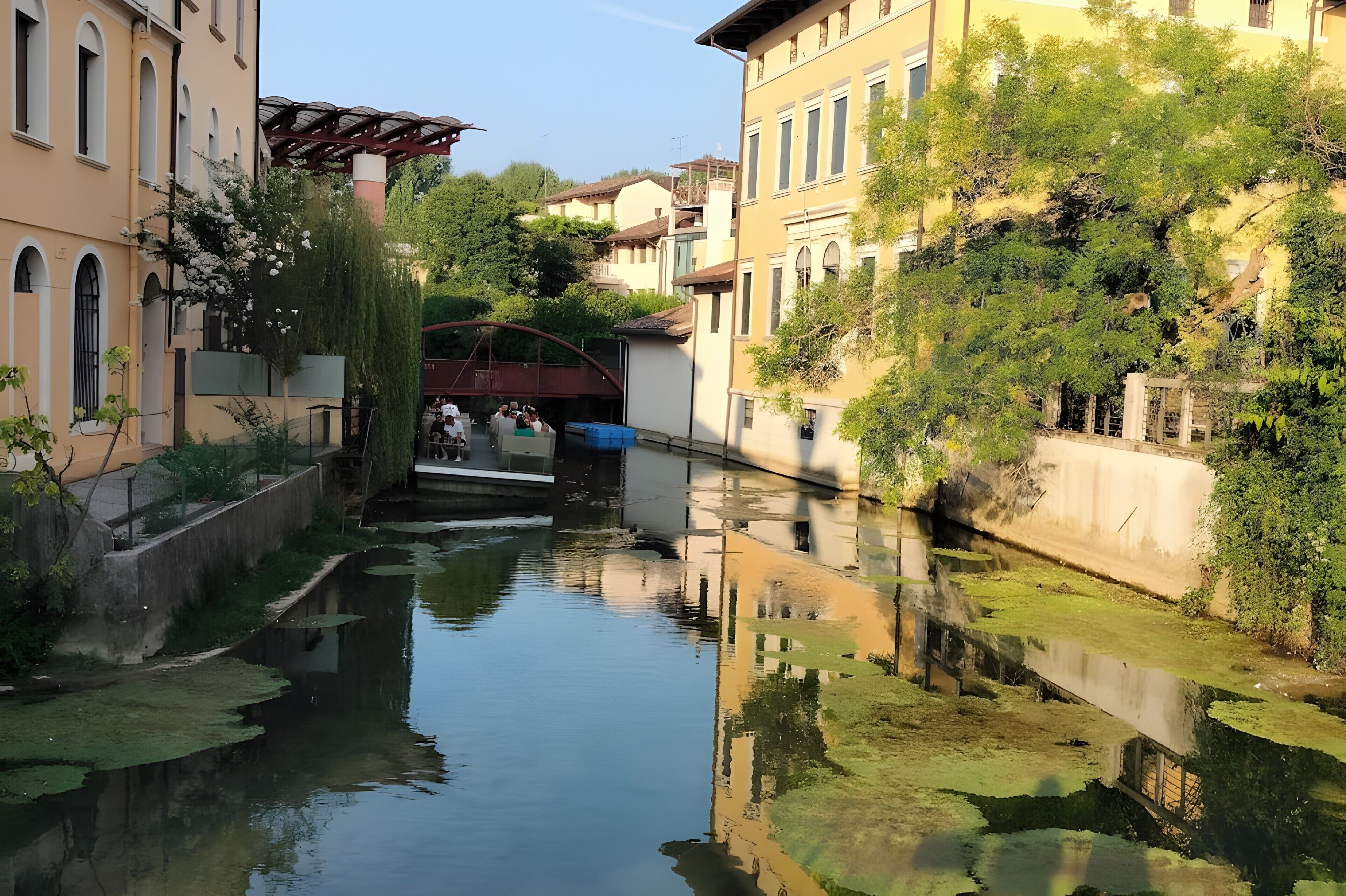 Un canal bordé de bâtiments des deux côtés, un petit pont et un arbre aux fleurs blanches.