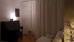 Una habitación con un piano, un televisor, una pequeña mesa y un adorno, además de una cortina.