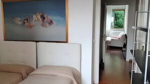 Un dormitorio con cama, un cuadro y vista a un área de estar con sofá y ventana.