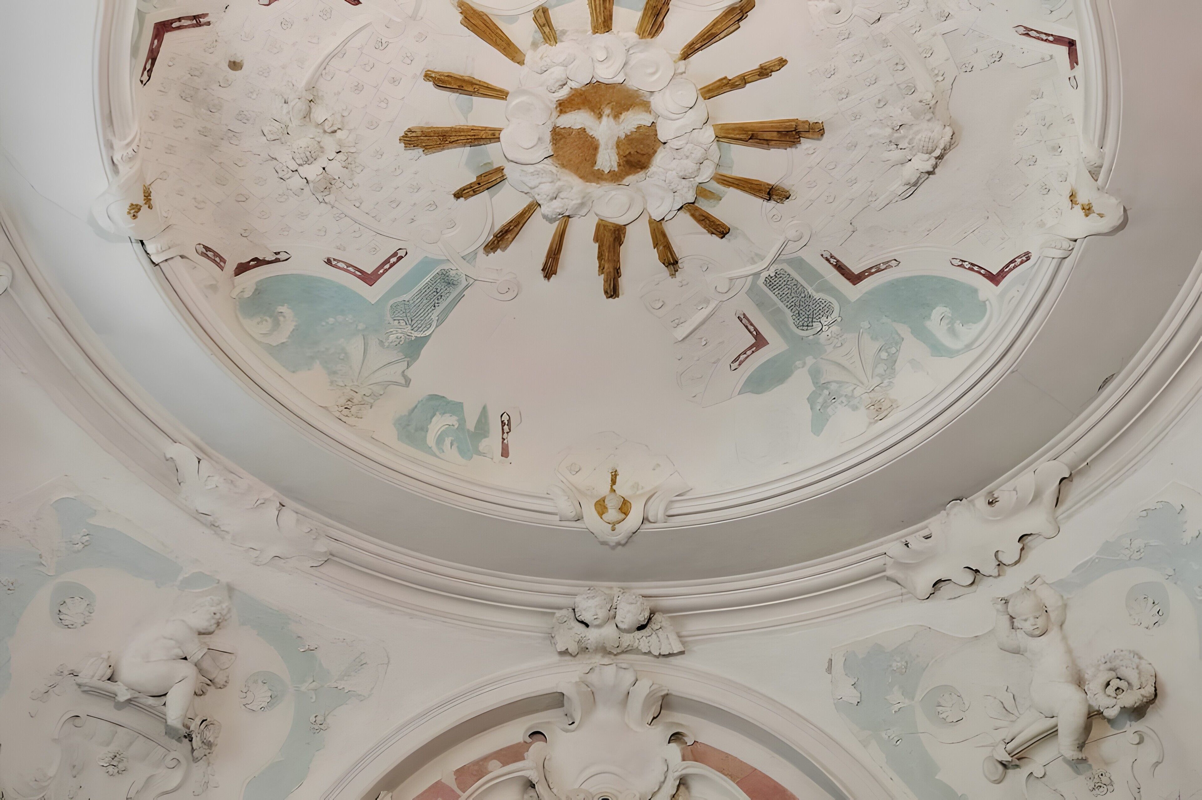 A ceiling with intricate plasterwork, including a central sunburst design and surrounding decorative elements.