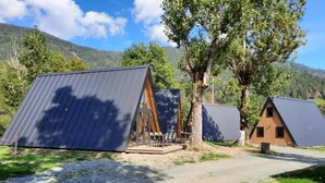 A modern, eco-friendly cabin with a sloped roof, surrounded by lush greenery and a mountainous backdrop. - Parc Sonnleiten - Edelhert (Gnesau)