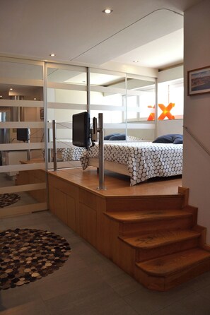 A modern bedroom with a bed, a TV, and a staircase leading to an upper level. - Beautiful studio with AC in enchanting Estoril perfect for getaway. (Estoril)