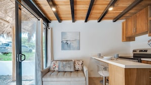 A modern kitchen with wooden cabinets, a dining area with a sofa, and a large window offering a view of the outside. - Playa Grande Apartment Loft # 1 - Starlink WiFi - Walk to Beach - Sleeps 3 (Santa Cruz (Playa Grande is a beach community within the Santa Cruz canton))