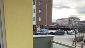 Un balcon avec une petite table, un mur jaune et une vue sur un parking et des immeubles.