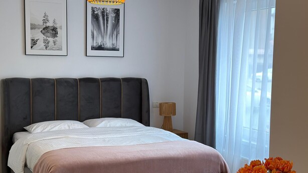 Une chambre à coucher avec un lit, une table de chevet, une lampe, une chaise et un vase avec des fleurs.