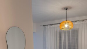 Un salon moderne avec un canapé beige, un miroir rond, une petite table ronde et un luminaire suspendu.