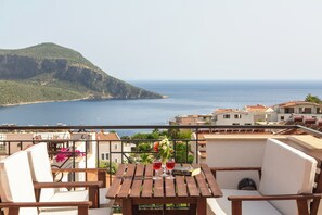Ein Balkon mit Holztisch, zwei Stühlen und Blick auf das Meer und ein Bergmassiv.
